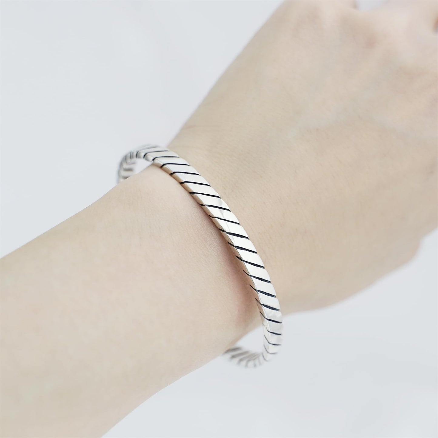 Oxidised rope cuff bangle on wrist, silver-toned diagonal rope ridged band