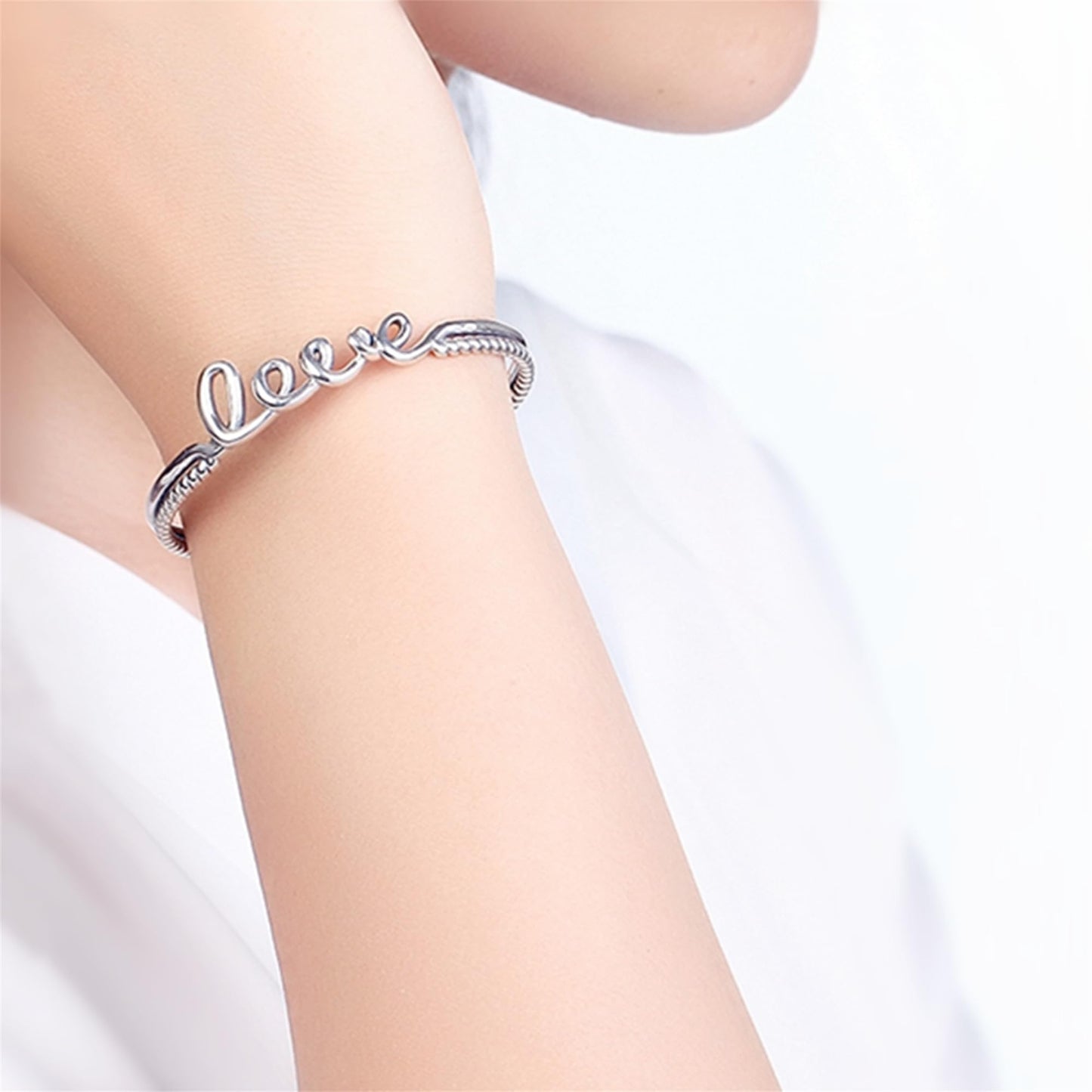 Silver rope-cuff bracelet worn on wrist with 'Love' script and knot detail.
