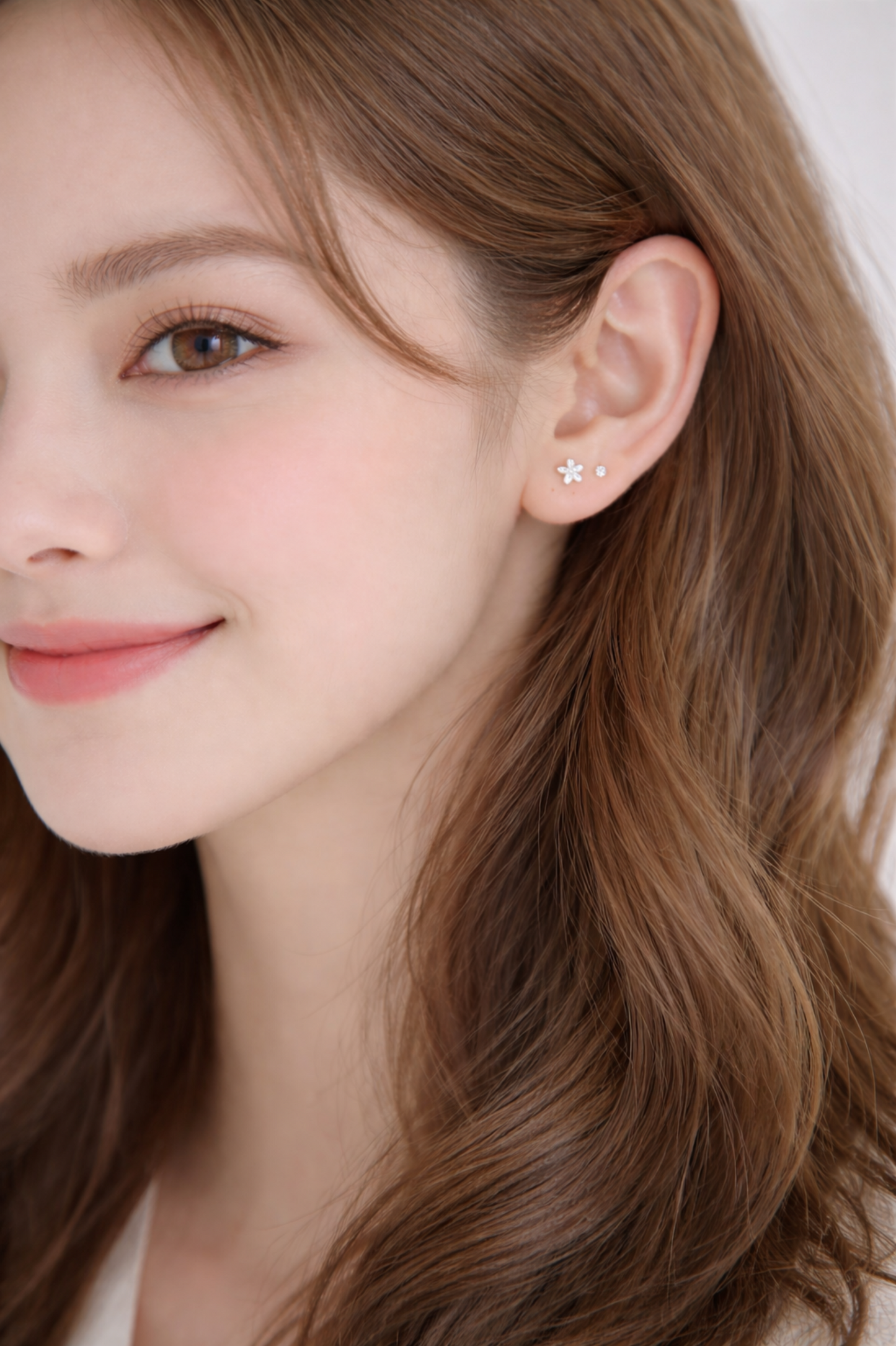 Silver flower stud earrings on ear, small five-petal bloom and matching stud.