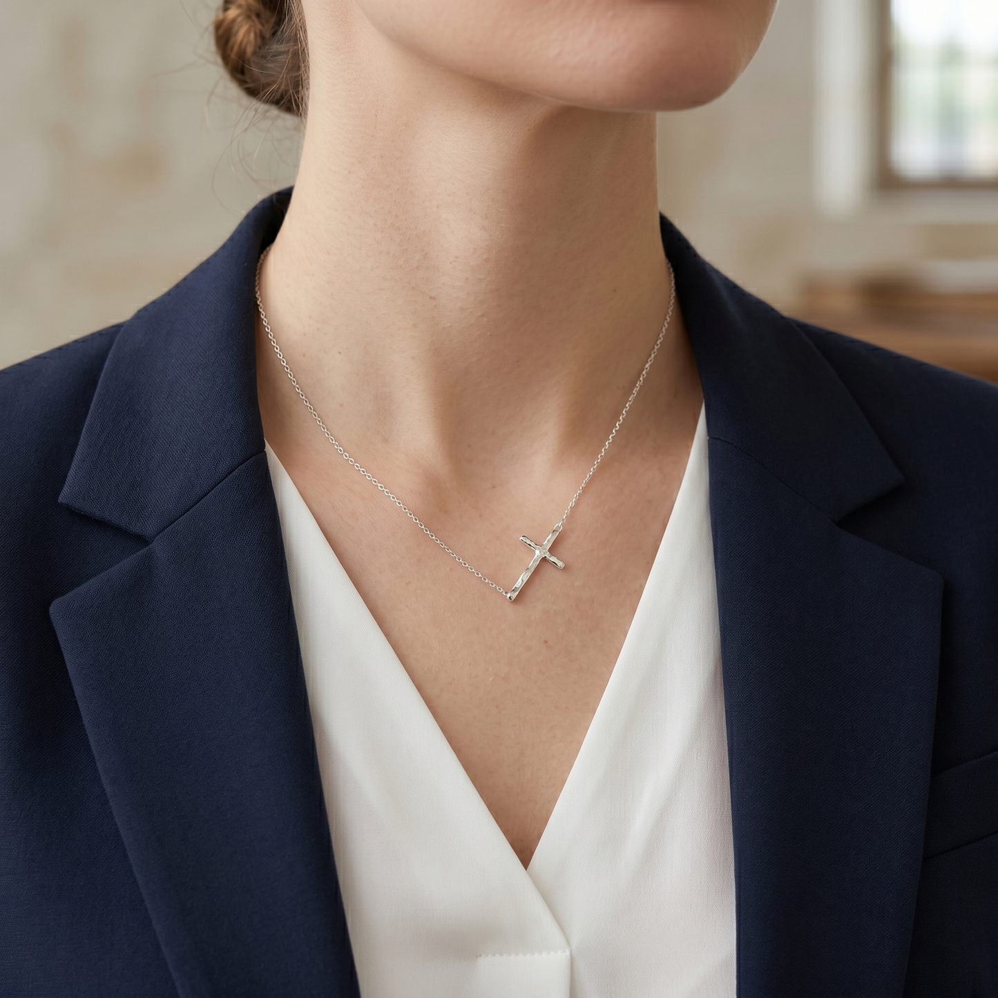 Silver cross pendant necklace worn on a woman’s neck, polished cross pendant centered.