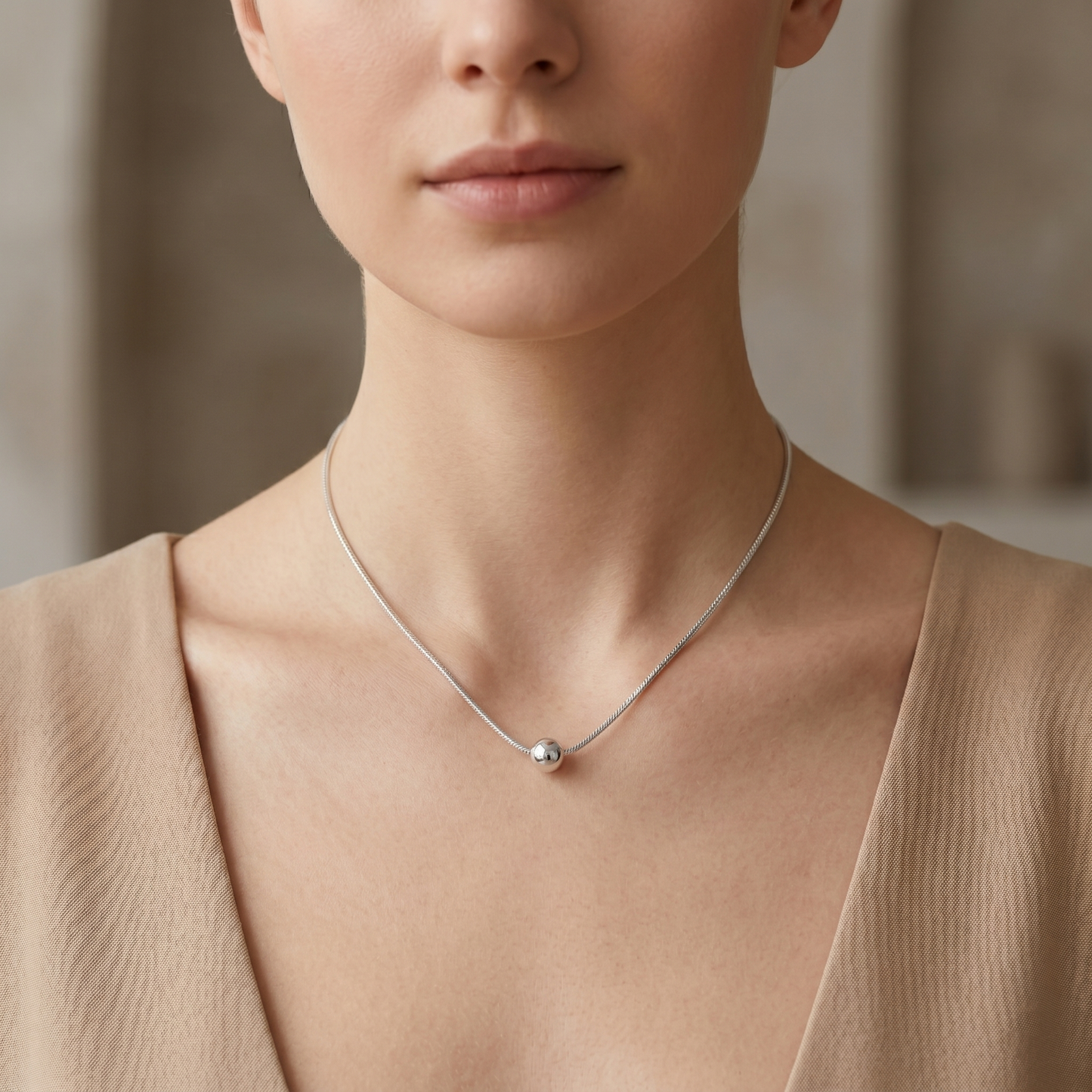 Polished ball pendant necklace worn at collarbone with round pendant on chain.