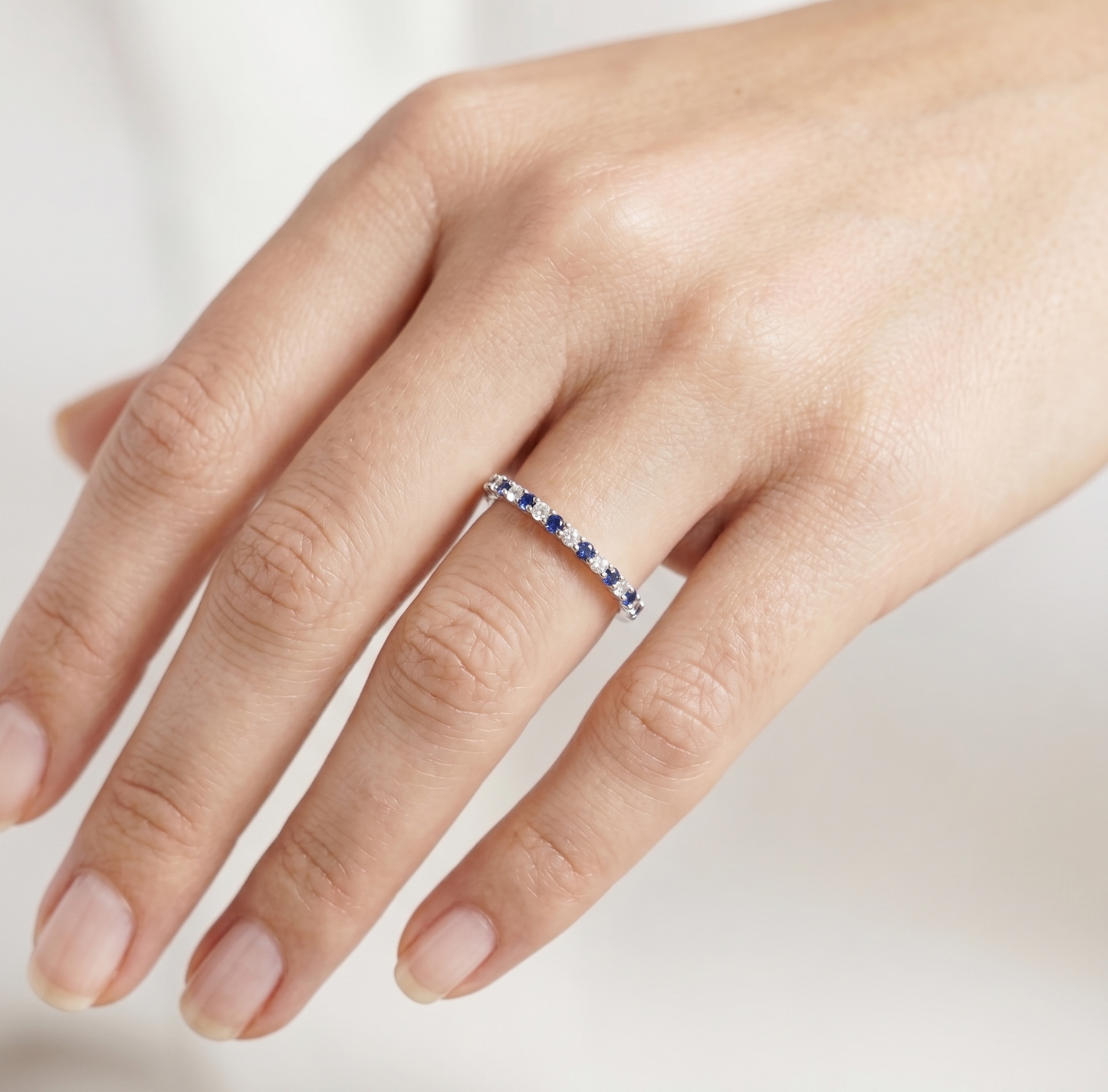 Sapphire eternity band ring on finger with blue and clear stones in silver setting