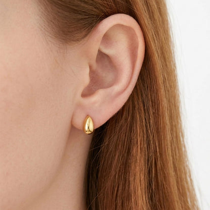Gold teardrop stud earrings on a model’s ear, smooth oval drop fronts
