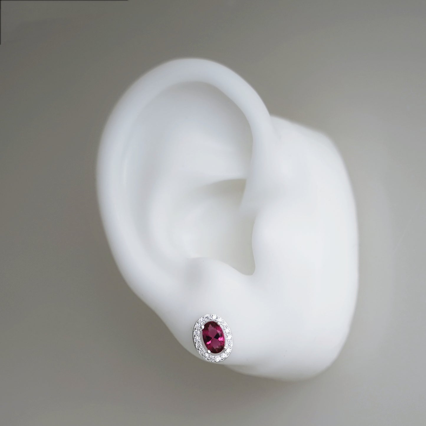 Ruby-red CZ stud earring with oval center stone and silver halo setting