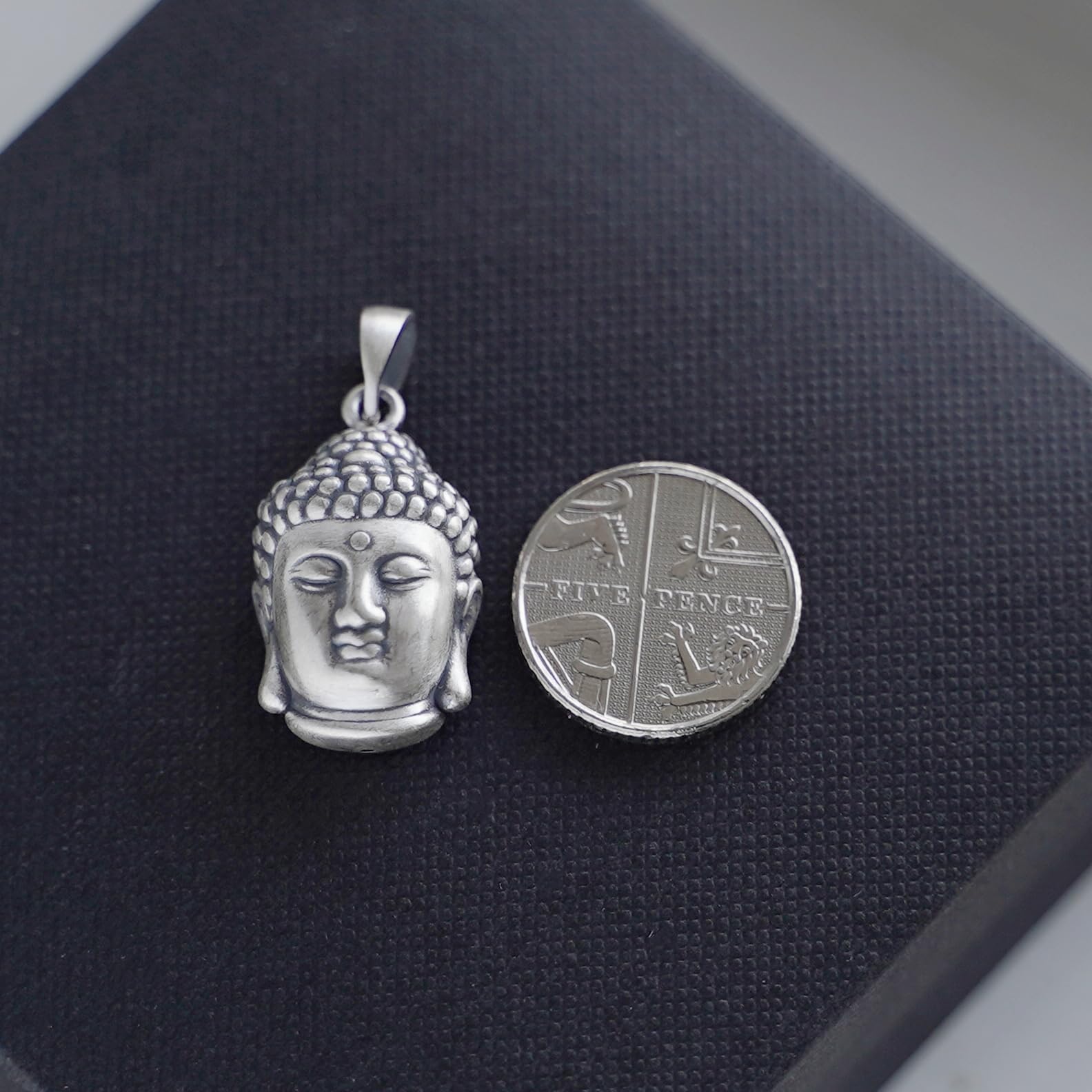 Buddha head pendant with detailed face; shown next to coin for size, silver-tone