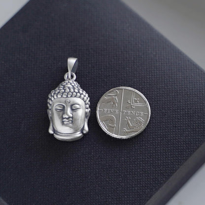 Buddha head pendant with detailed face; shown next to coin for size, silver-tone