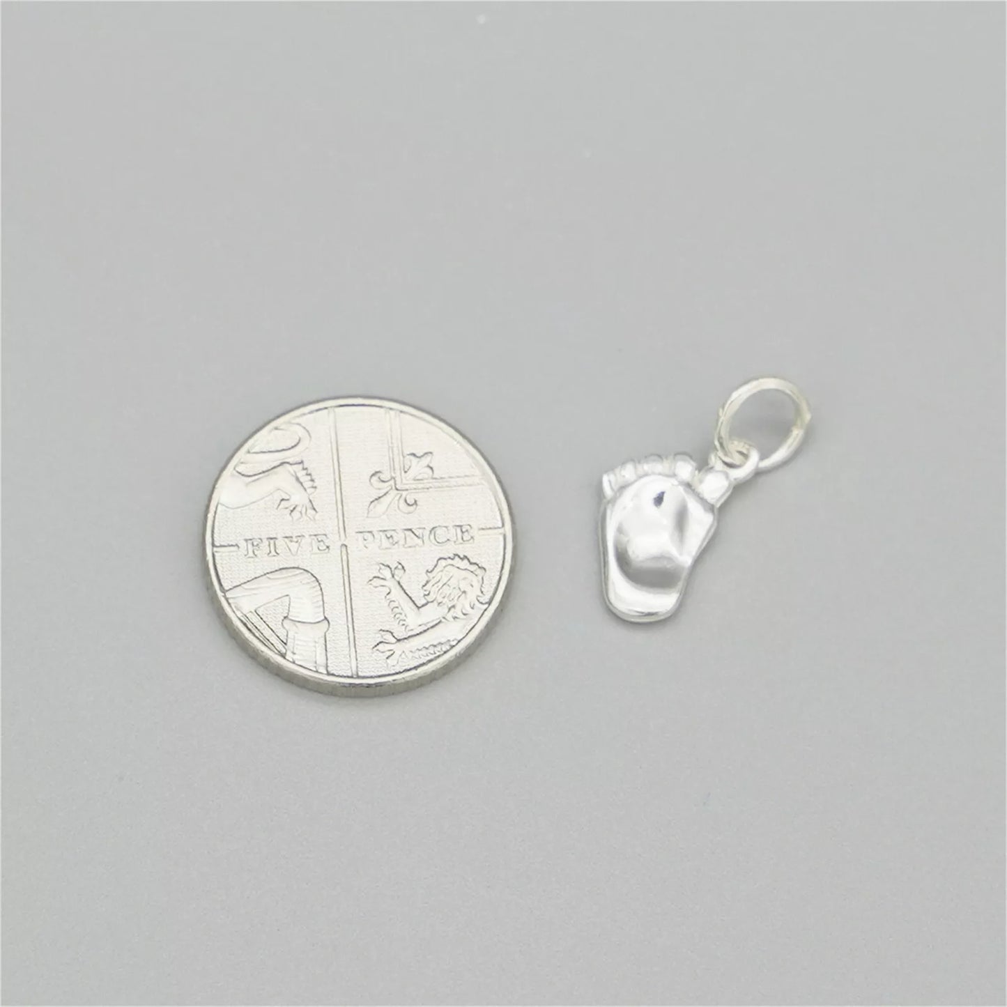 Silver baby foot charm next to a coin for size, with enamel sole detail