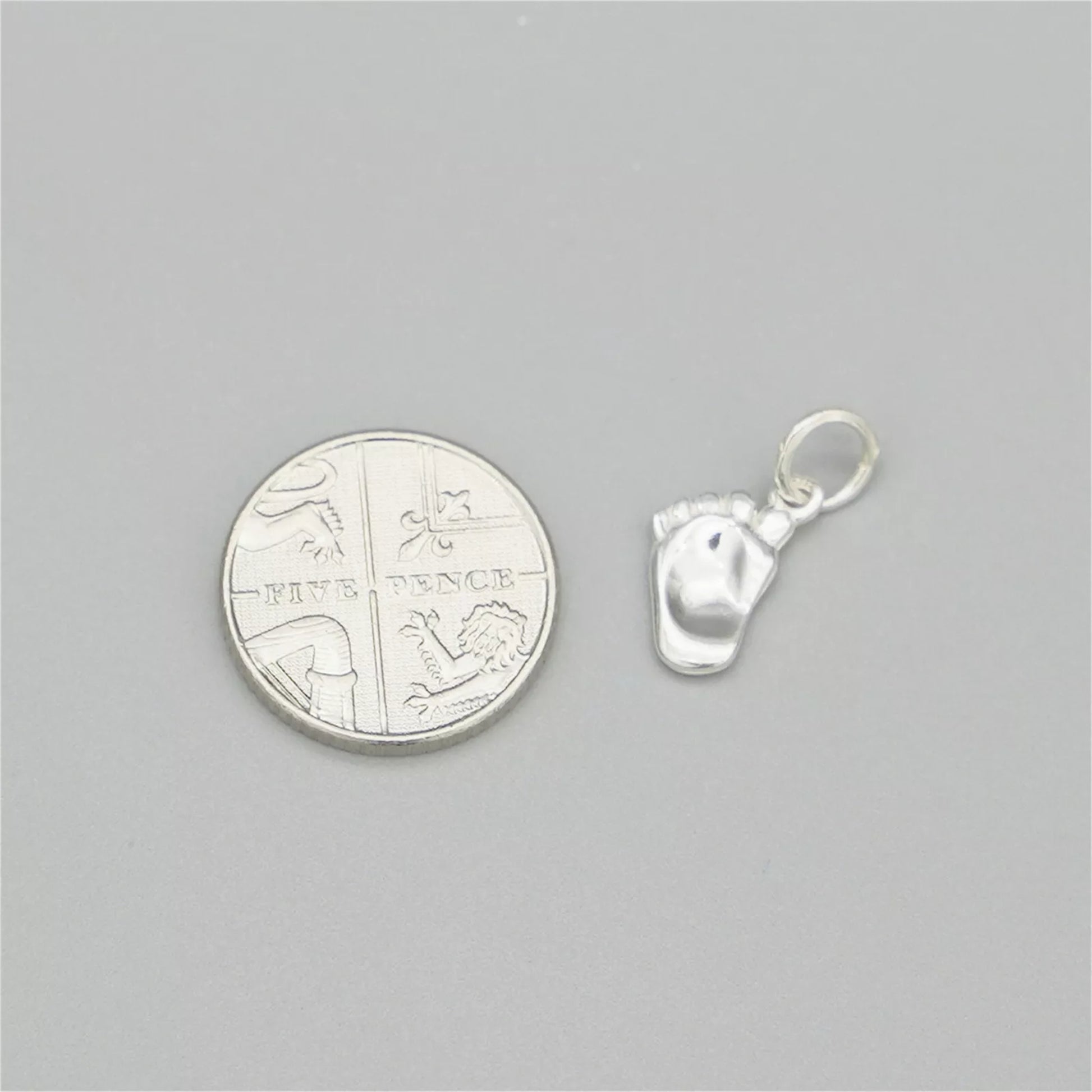 Silver baby foot charm next to a coin for size, with enamel sole detail