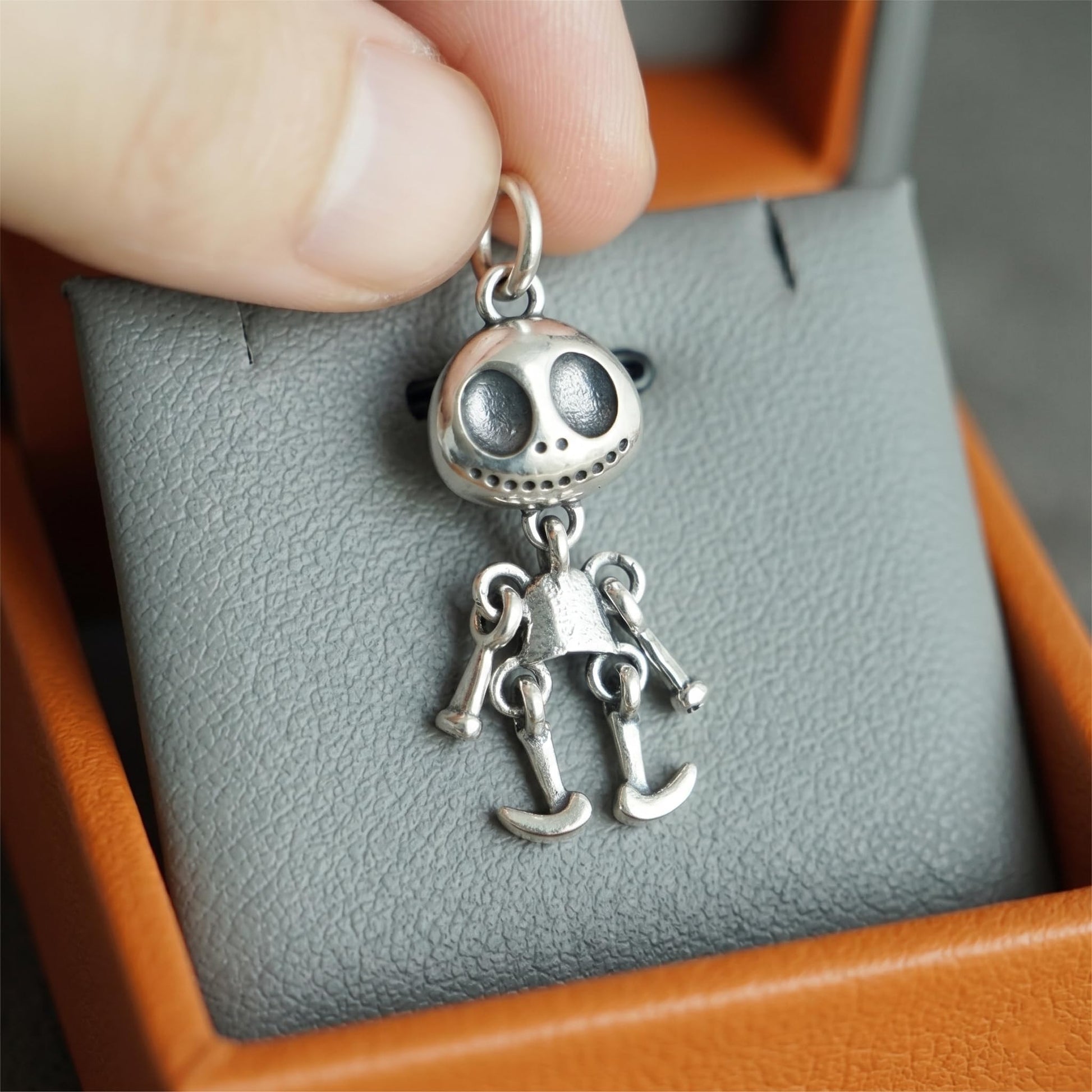 Hand holding a movable ghost face pendant, silver-tone with dangling legs