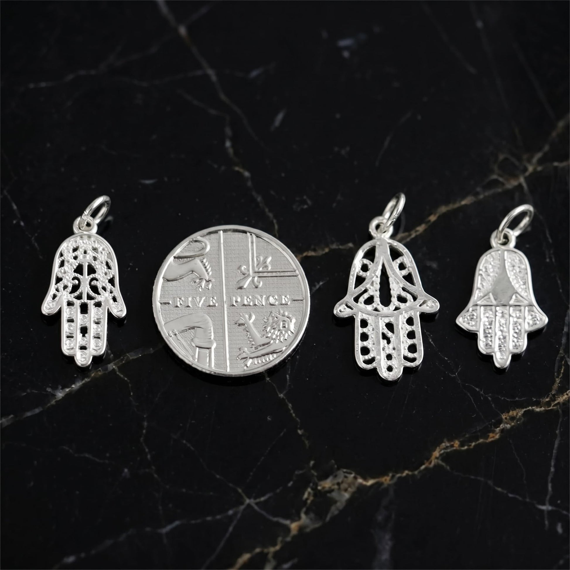 Silver hamsa hand charms, plus other pendants, displayed with a coin for scale