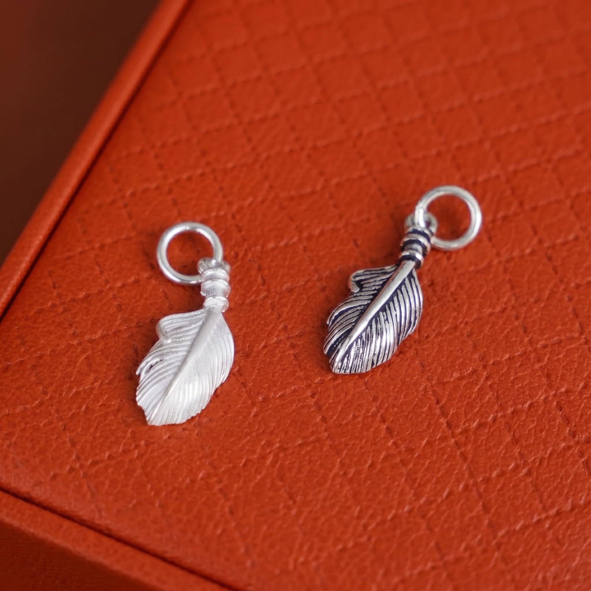 Silver feather wing charm with loop and striped feather detailing on top.