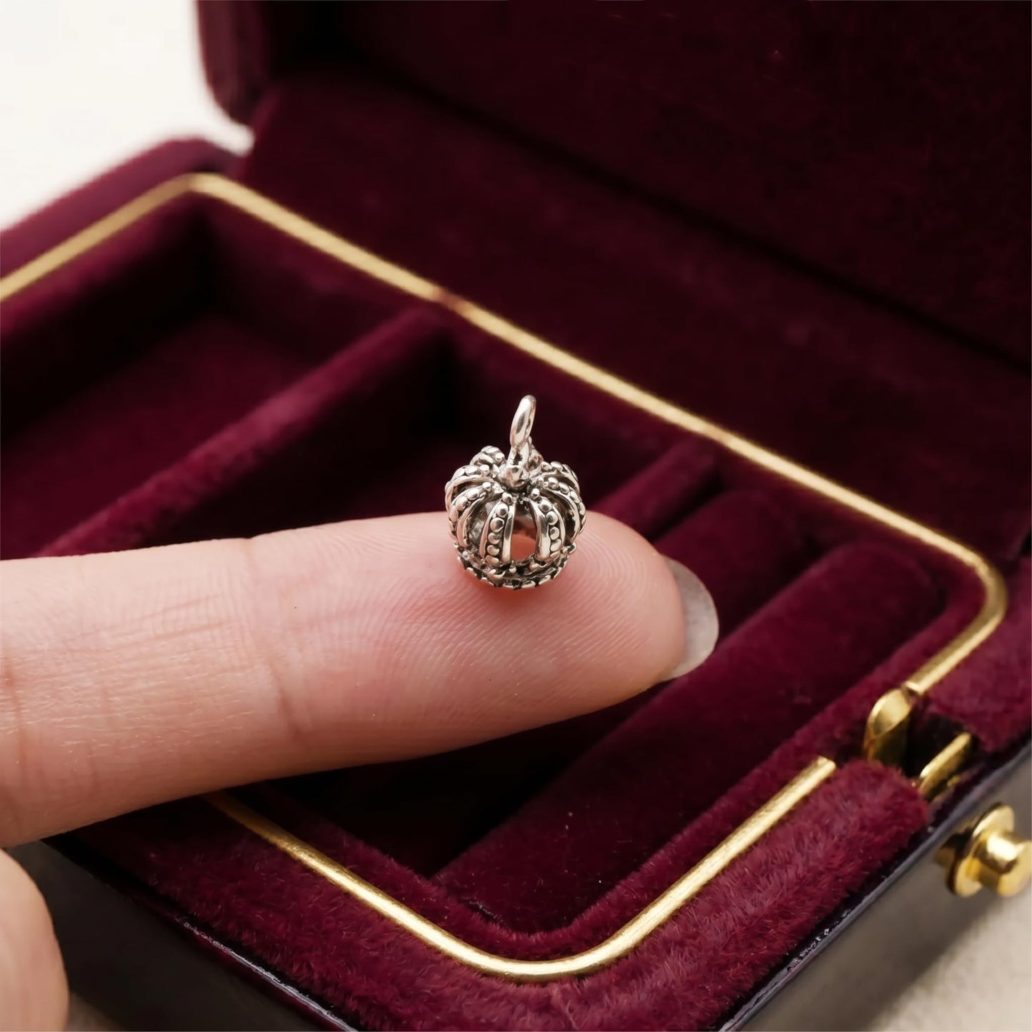 Single mini crown charm on fingertip, silver-tone crown with loop bail