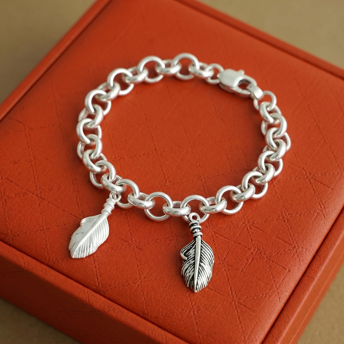 Silver chain bracelet with two feather wing charms and dangling loops.
