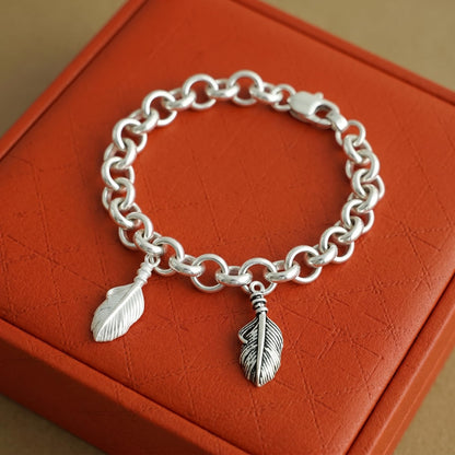 Silver chain bracelet with two feather wing charms and dangling loops.