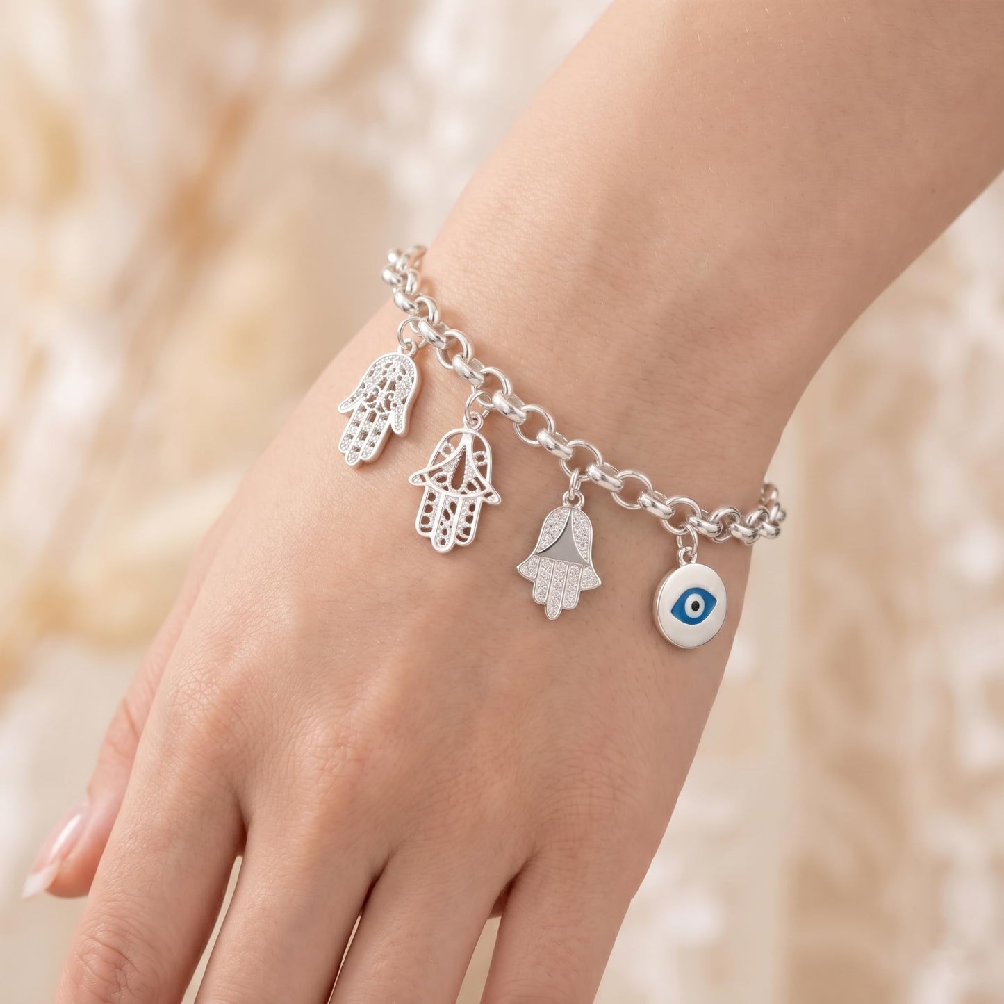 Silver charm bracelet with hamsa hand charms and a blue eye charm on wrist