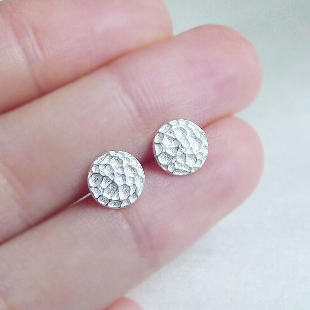 Pair of silver hammered disc stud earrings held in fingers, round textured faces