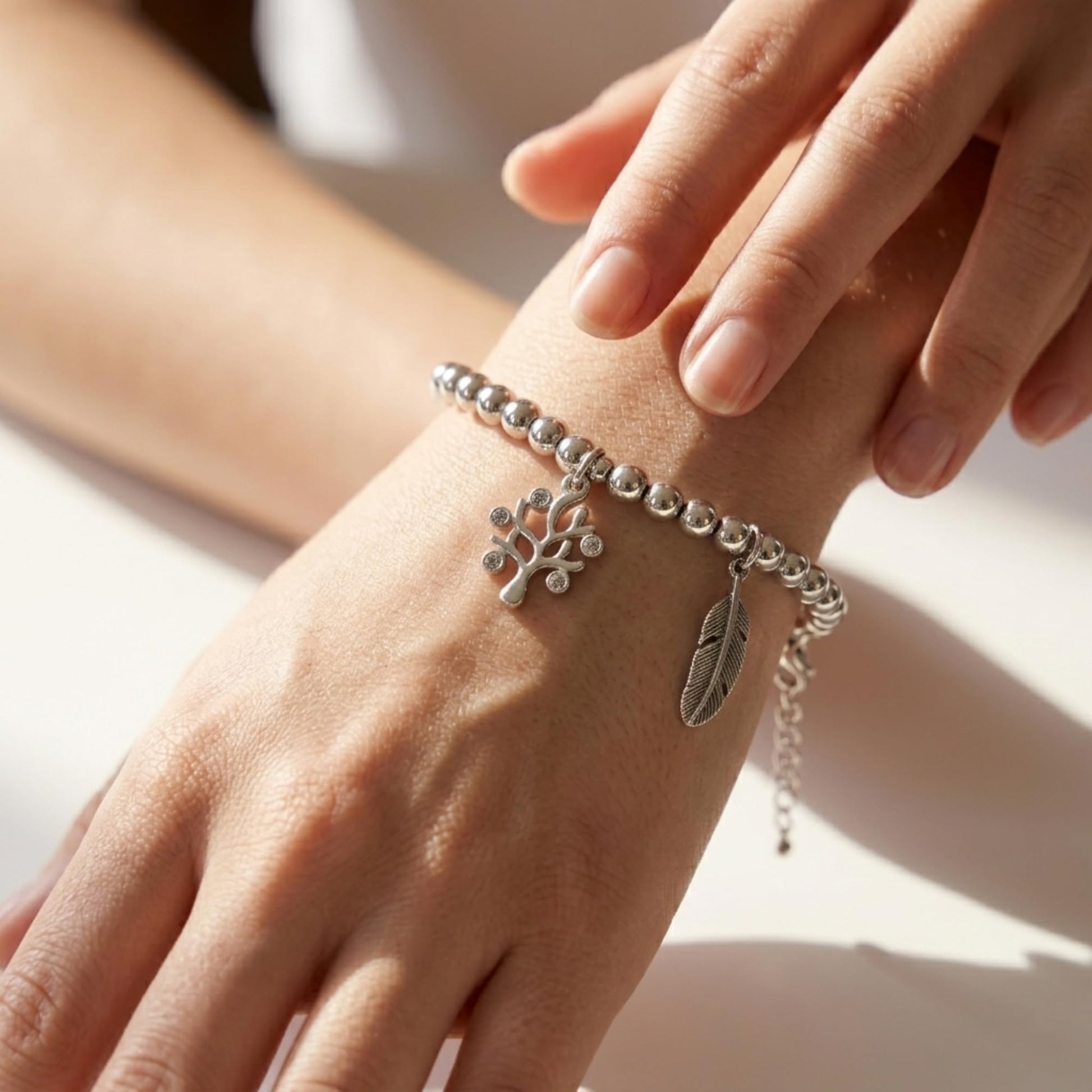 Tree of Life charm on a silver bead bracelet on a wrist with leaf pendant