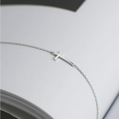 Silver-tone cross anklet bracelet with sideways cross charm, partial view.