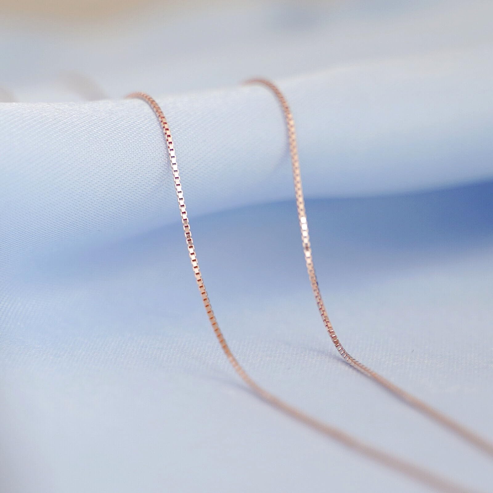 Rose gold-tone box chain necklace on fabric surface, close-up of links