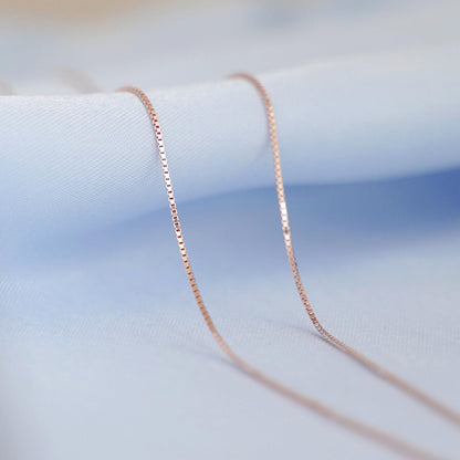 Rose gold-tone box chain necklace on fabric surface, close-up of links