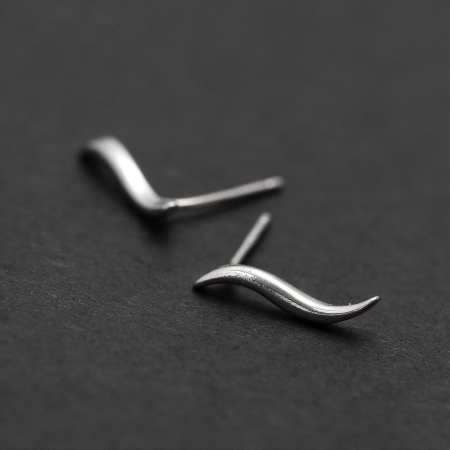 Silver wavy vine climber stud earrings, close-up of curved wave form