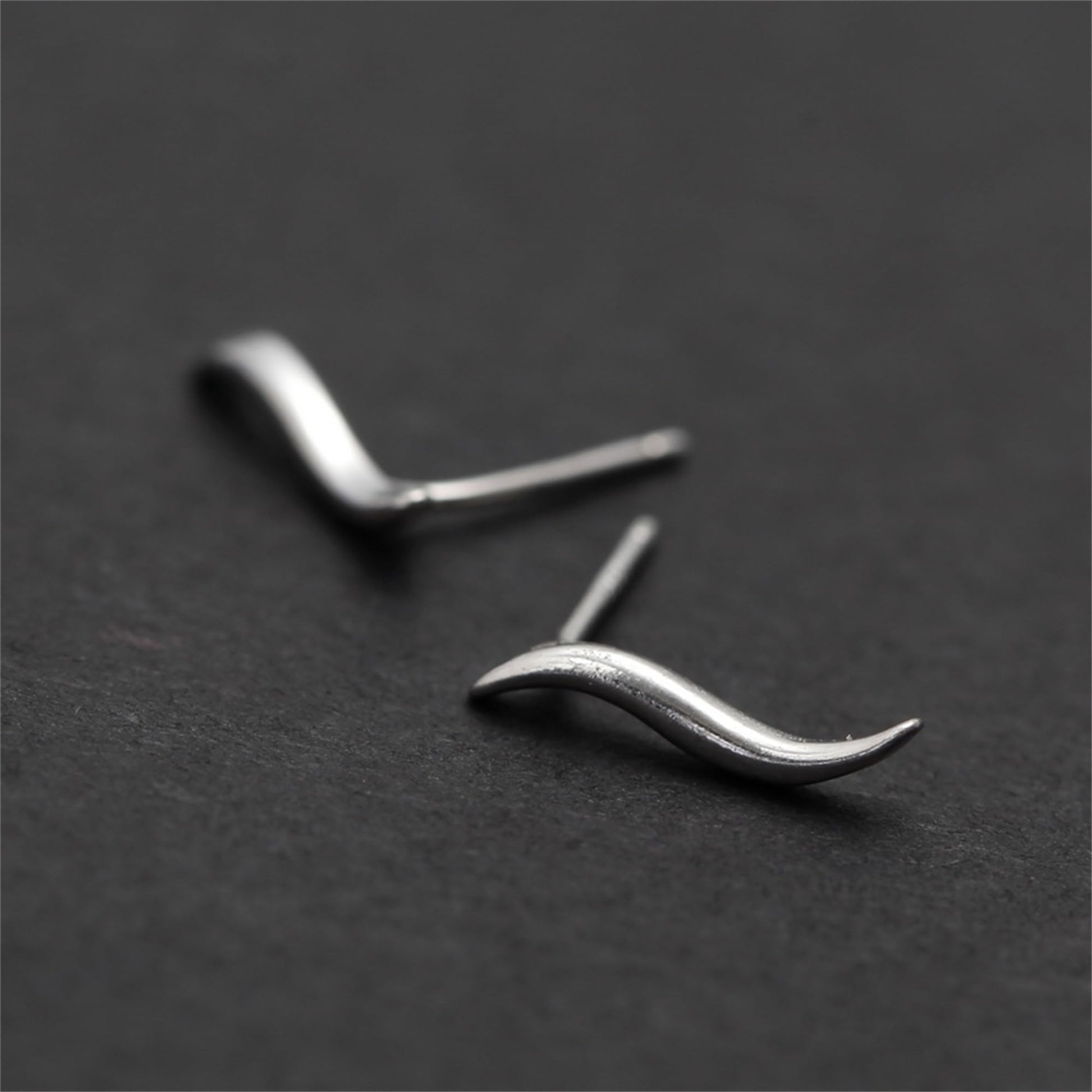 Silver wavy vine climber stud earrings, close-up of curved wave form