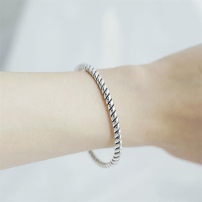Pearl twisted torque bangle on wrist with twisted silver band and white pearl charm.
