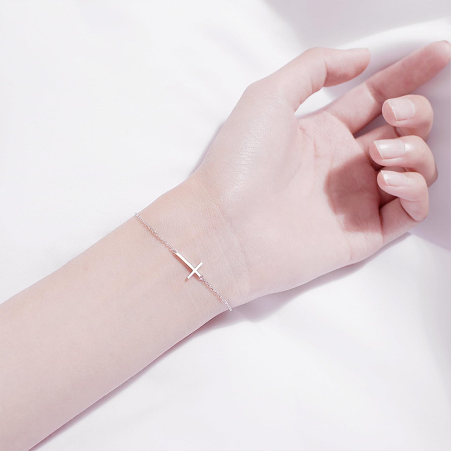Silver-tone cross anklet bracelet with sideways cross charm on hand.