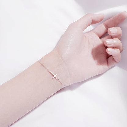 Silver-tone cross anklet bracelet with sideways cross charm on hand.