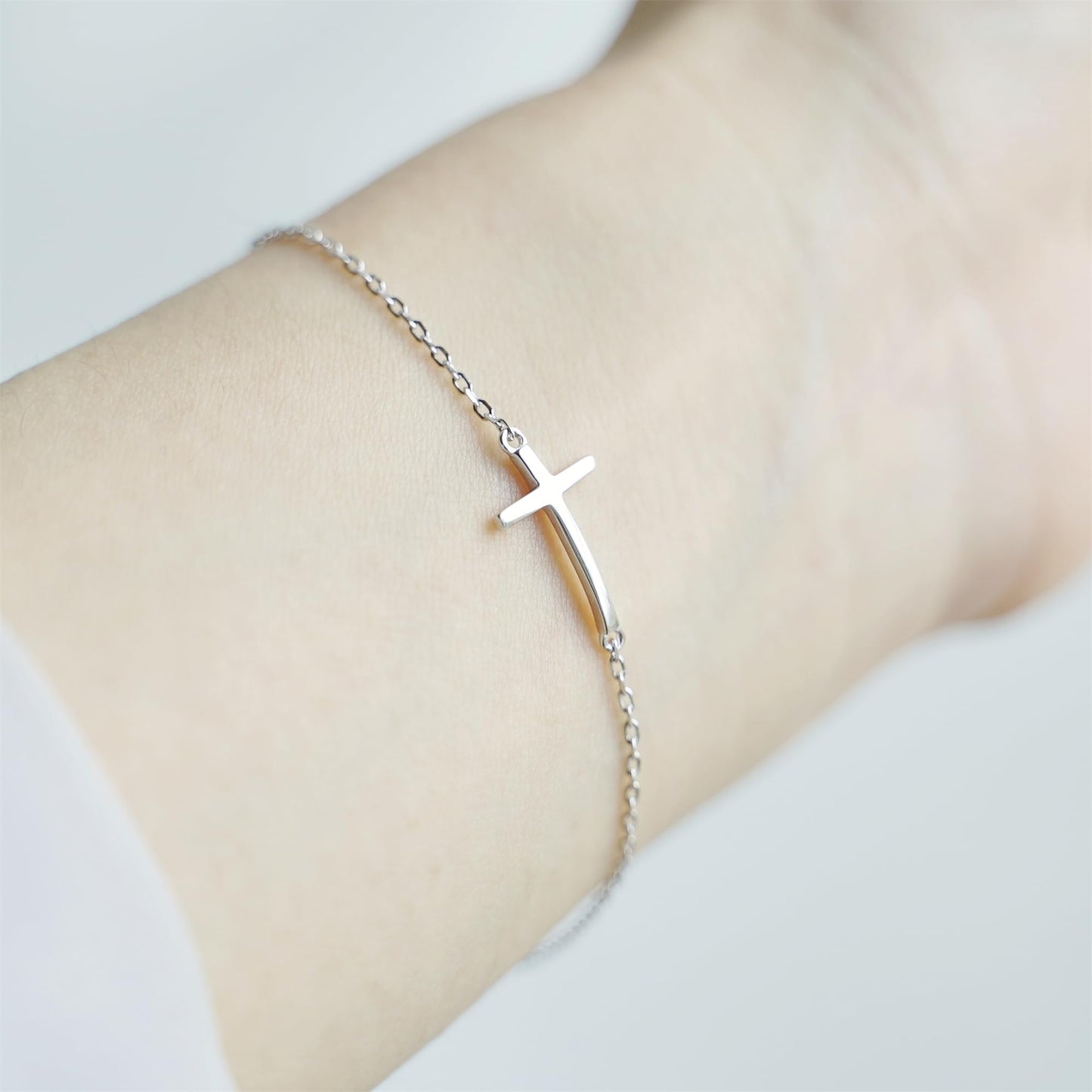 Silver-tone cross anklet bracelet with sideways cross charm on wrist.