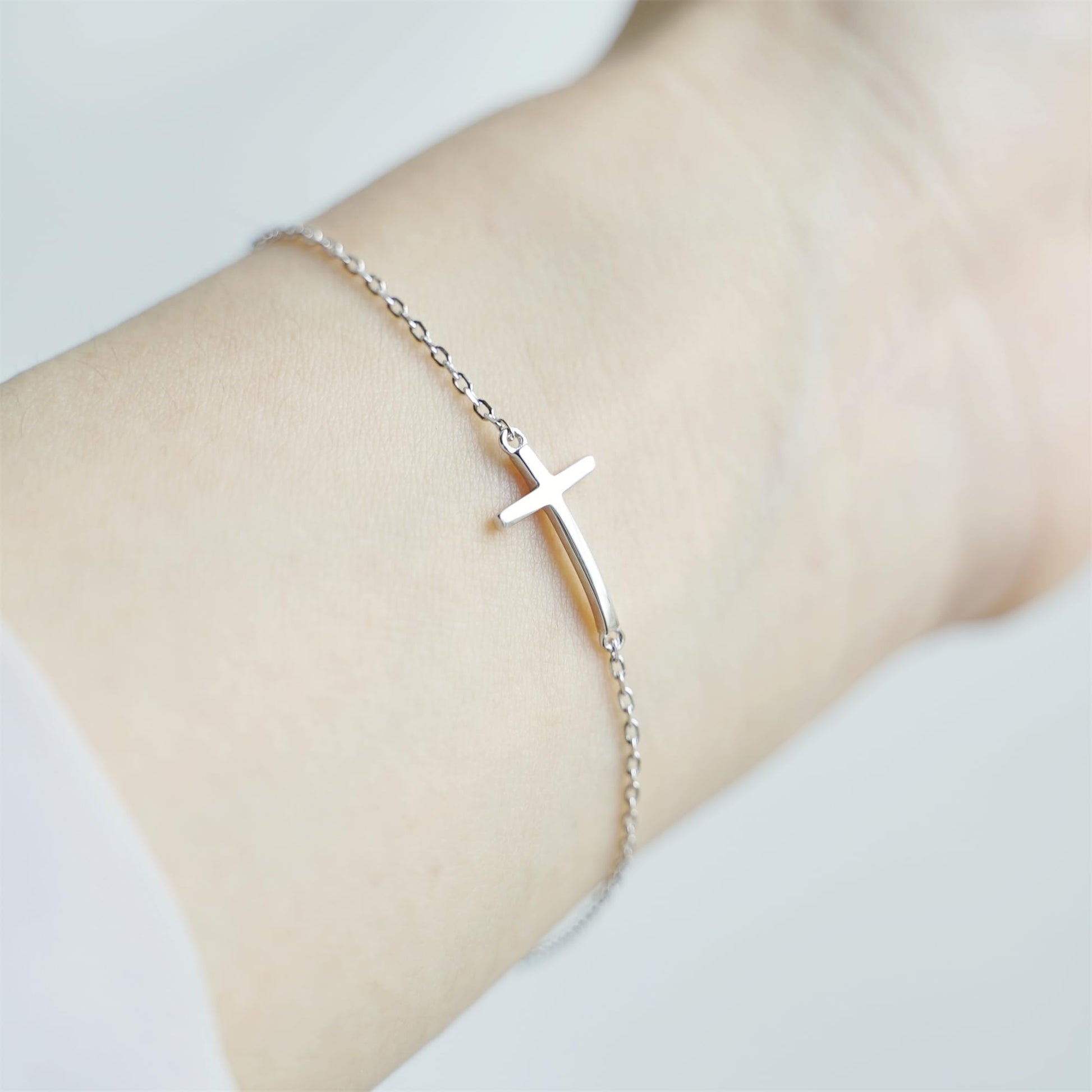 Silver-tone cross anklet bracelet with sideways cross charm on wrist.