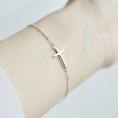 Silver-tone cross anklet bracelet with sideways cross charm on wrist.