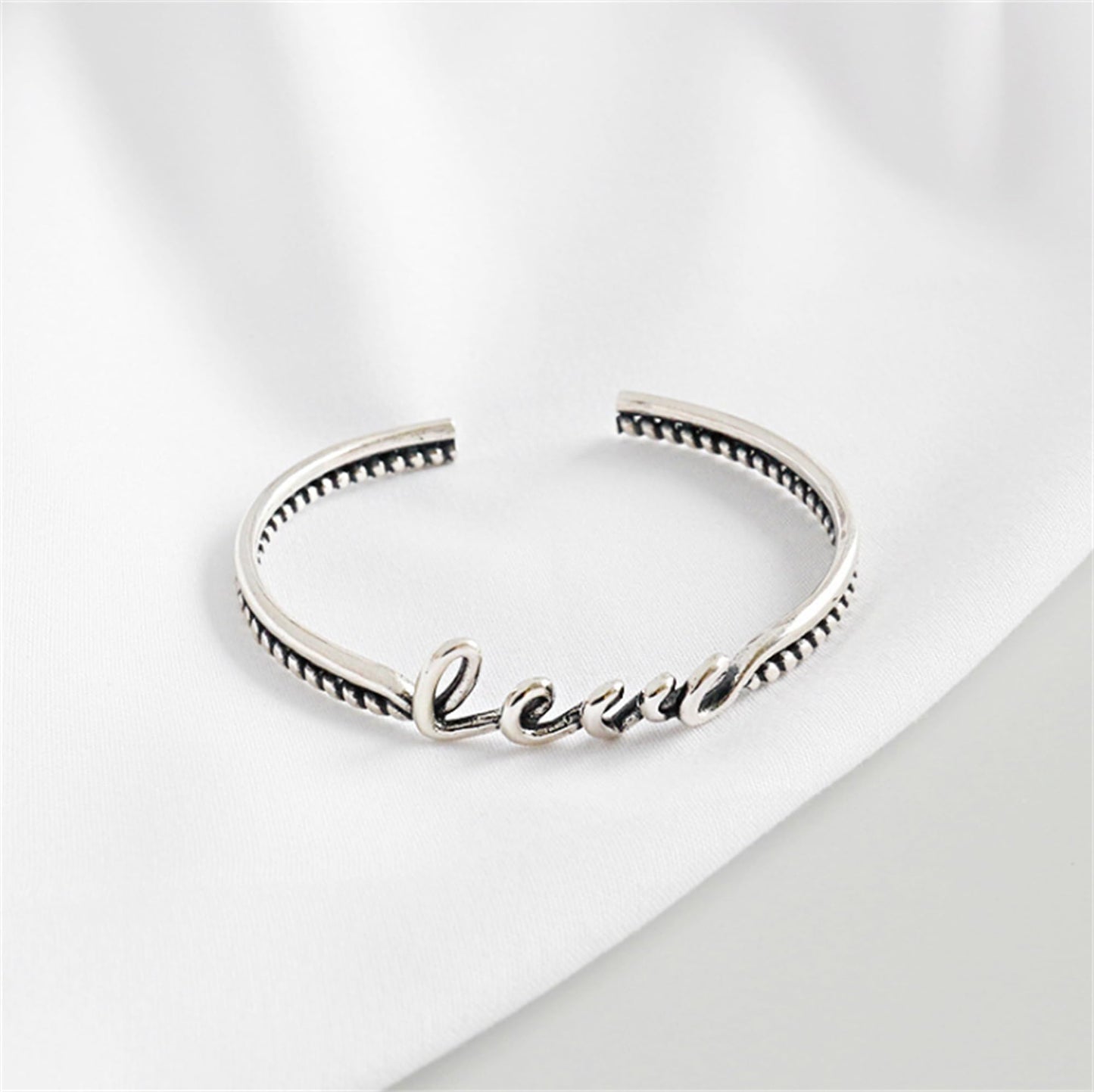 Silver rope-cuff bracelet with 'Love' script front and a textured beaded border.