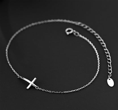 Silver-tone cross anklet bracelet with heart tag and sideways cross charm.