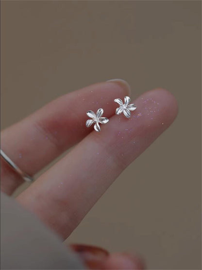 Silver lily flower stud earrings on fingertips, close-up