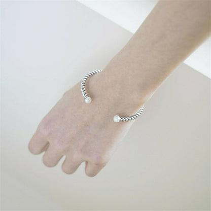 Pearl twisted torque bangle on hand with twisted silver band and white pearl beads.