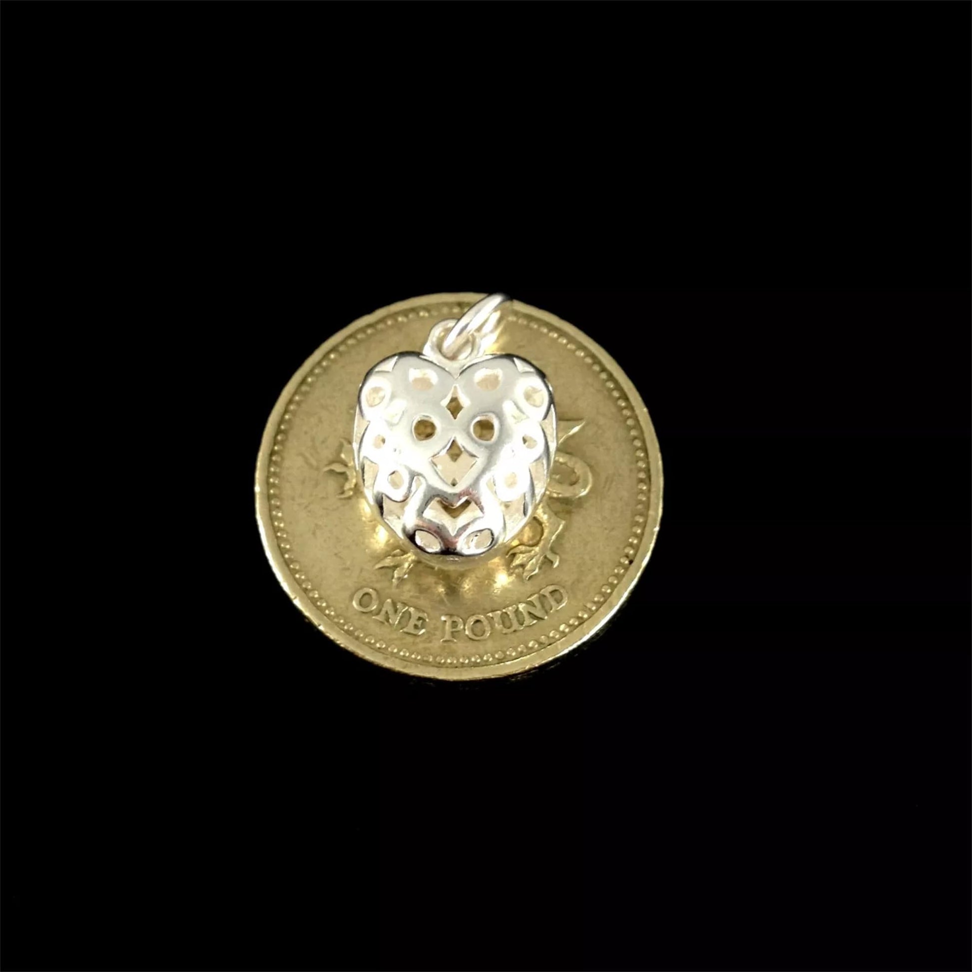Silver heart pendant charm with cut-out design, shown on a coin