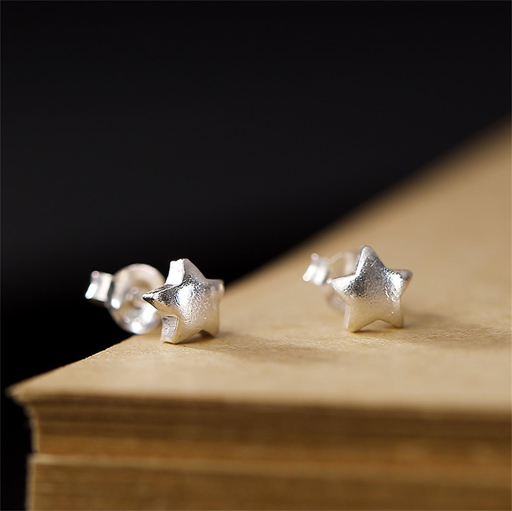 Five-point star stud earrings, silver-tone, on wooden surface