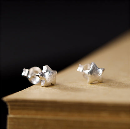 Five-point star stud earrings, silver-tone, on wooden surface