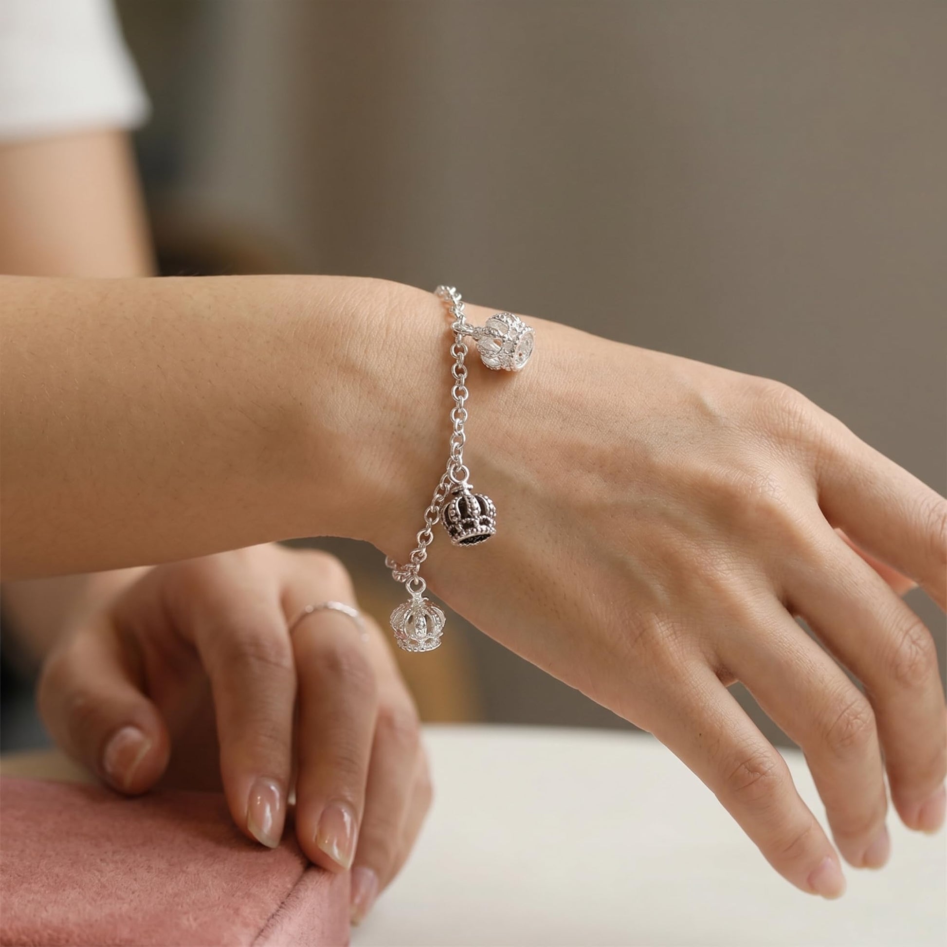 Crown charm bracelet on wrist, silver-tone chain with small crown pendant