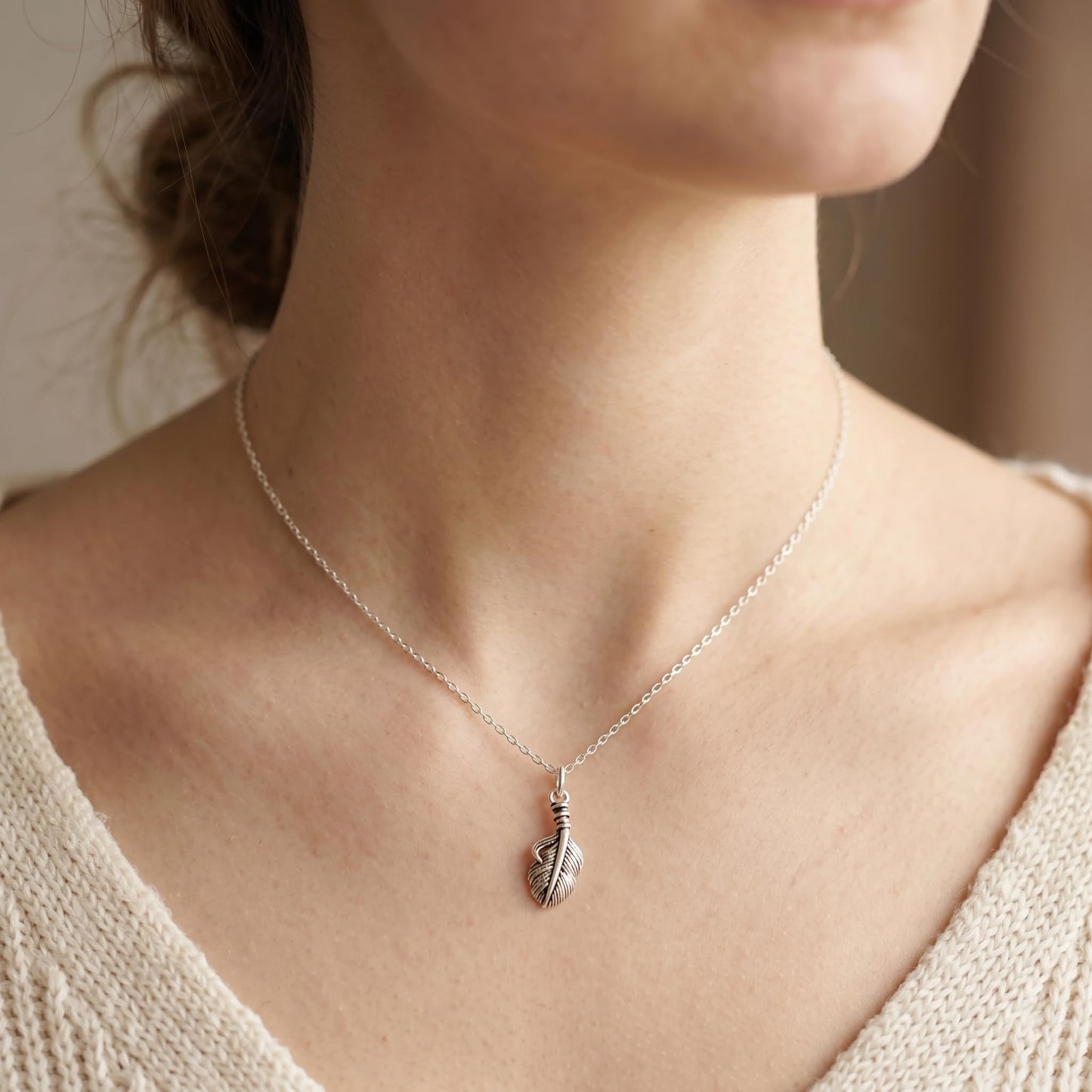 Silver necklace with a feather wing charm pendant and fine chain near neckline.