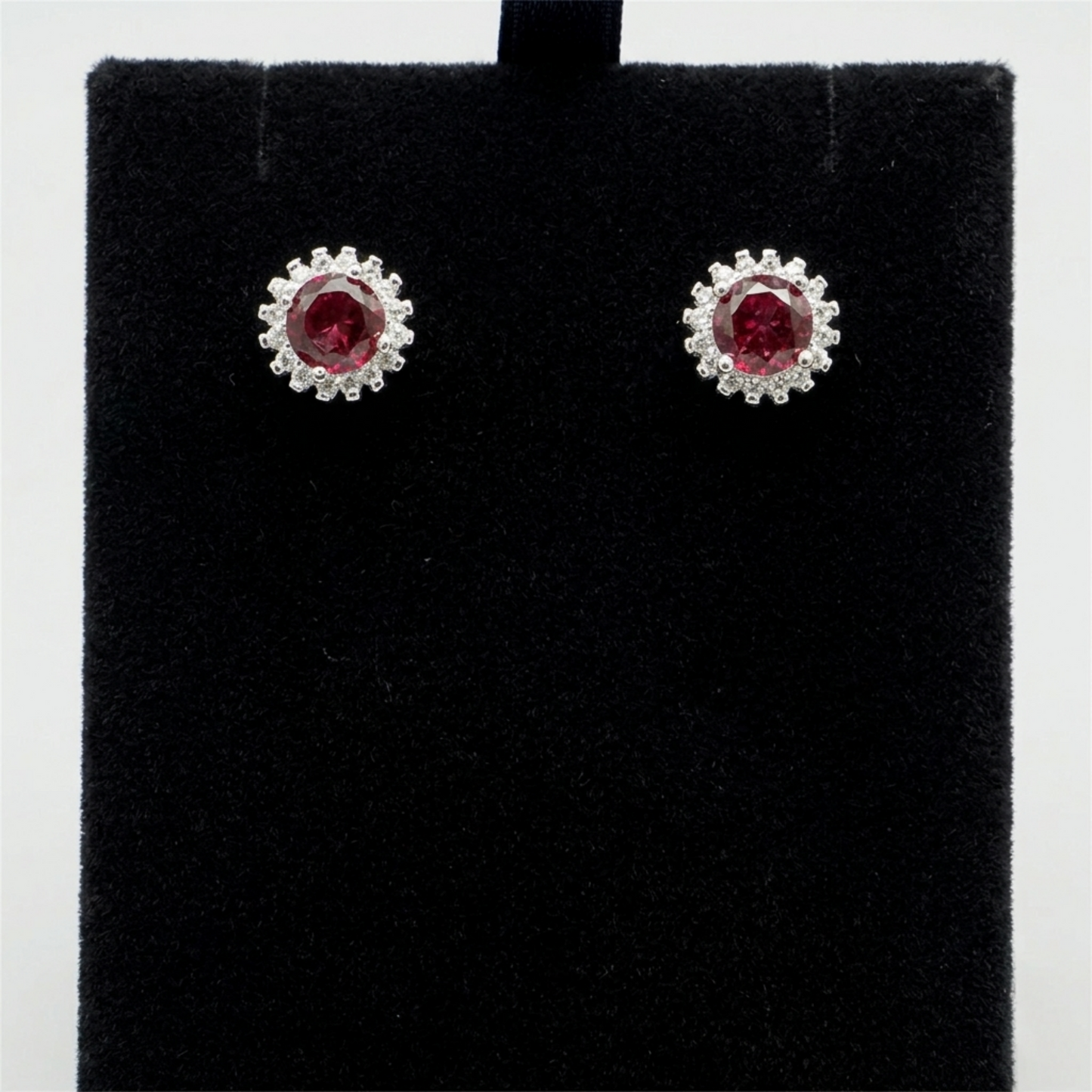 Round red gemstone stud earrings with halo of clear stones on dark display