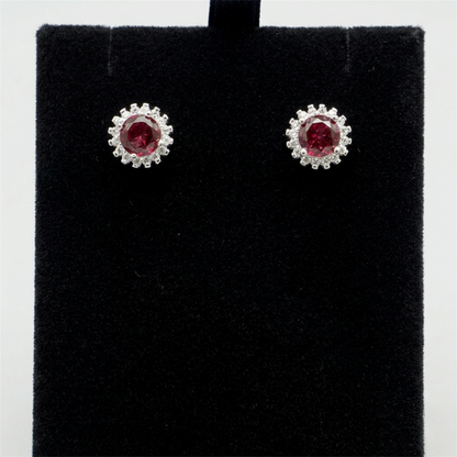 Round red gemstone stud earrings with halo of clear stones on dark display