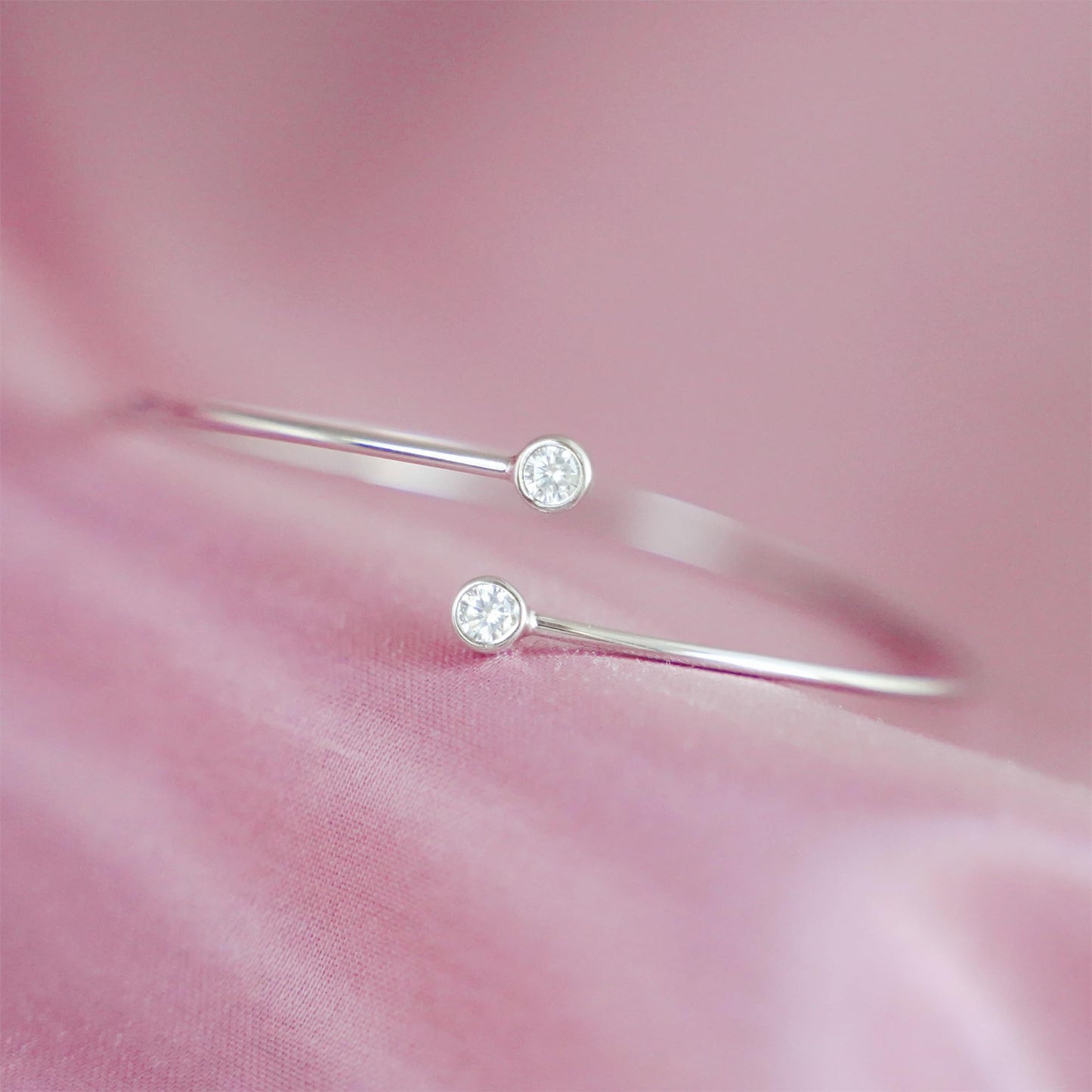Silver-tone torque bangle close-up showing two round CZ stones on slim bars