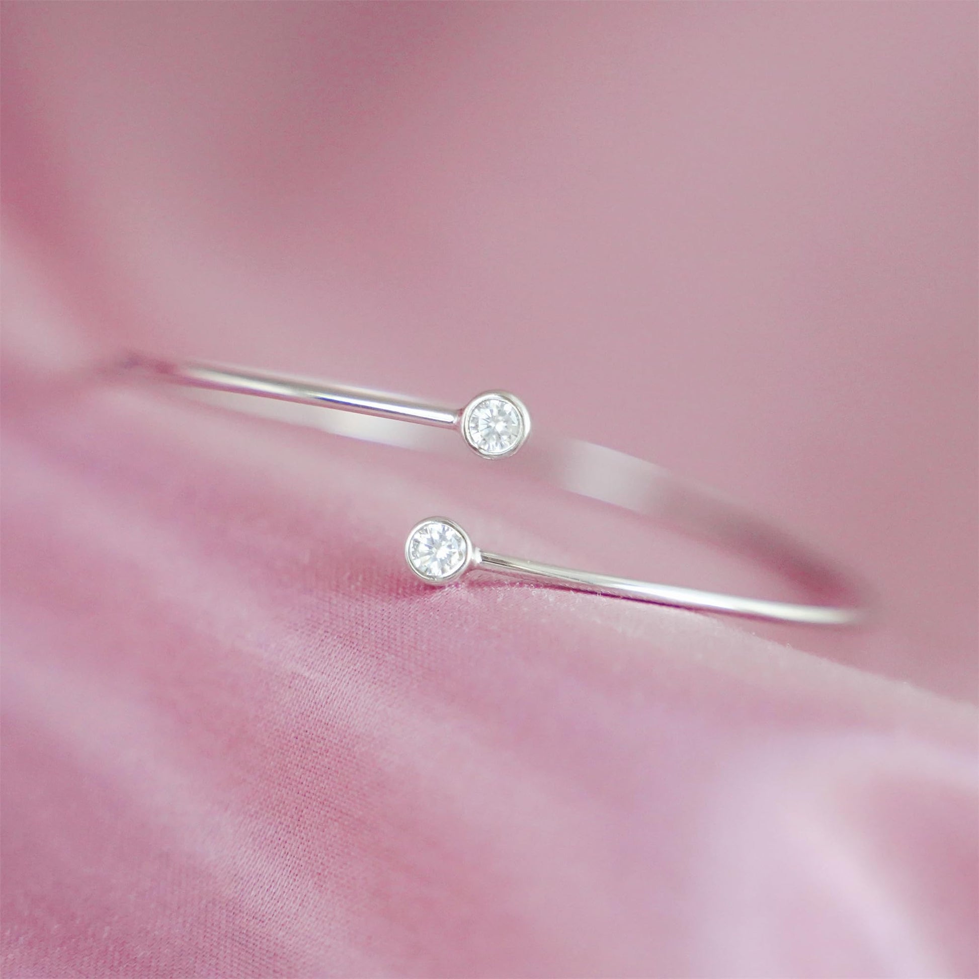 Silver-tone torque bangle close-up showing two round CZ stones on slim bars
