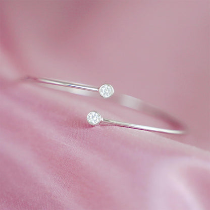 Silver-tone torque bangle close-up showing two round CZ stones on slim bars