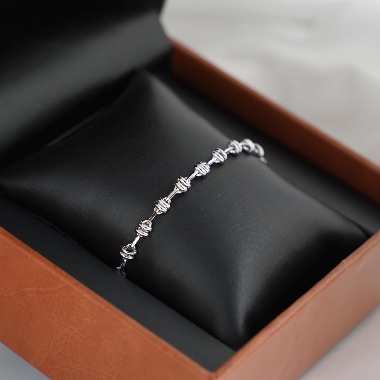 Silver-tone oval curb chain bracelet on black display cushion in a box