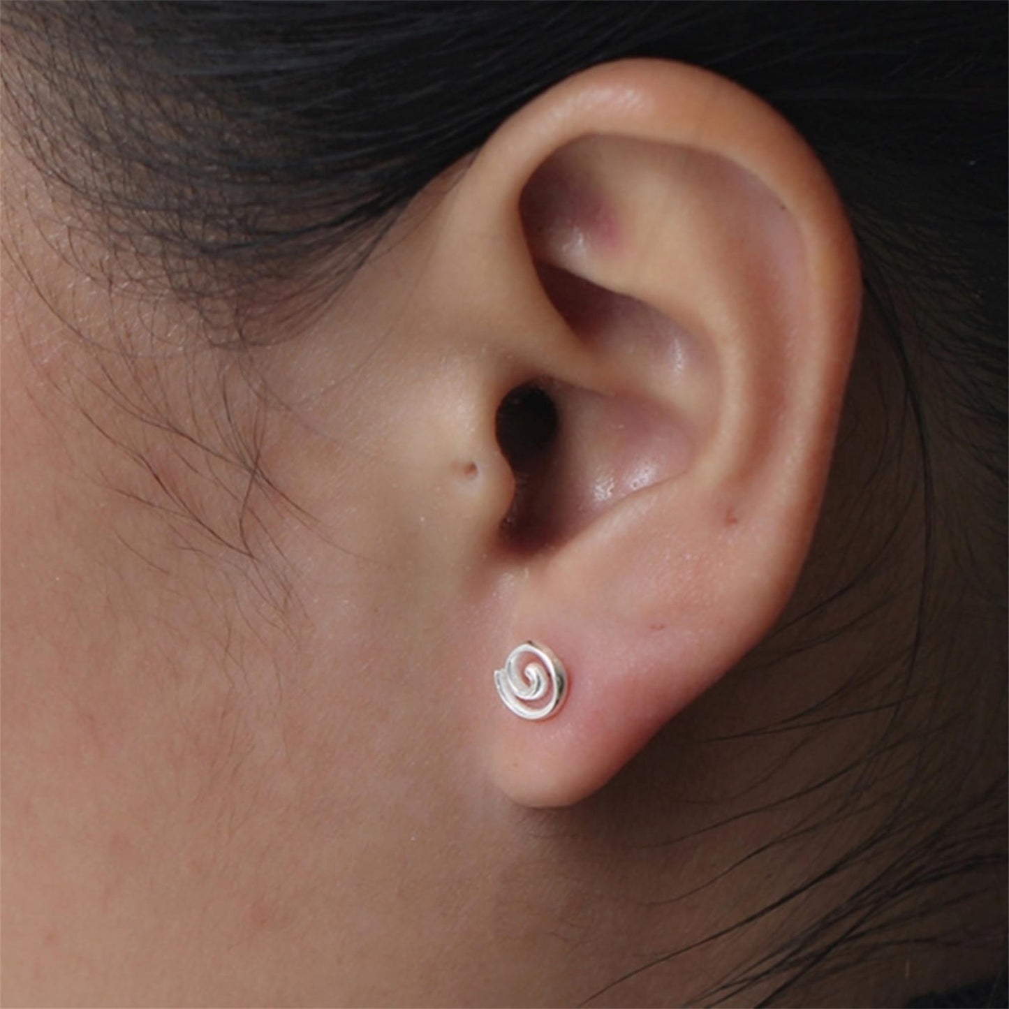 Silver spiral swirl stud earring on ear, small curled swirl design.