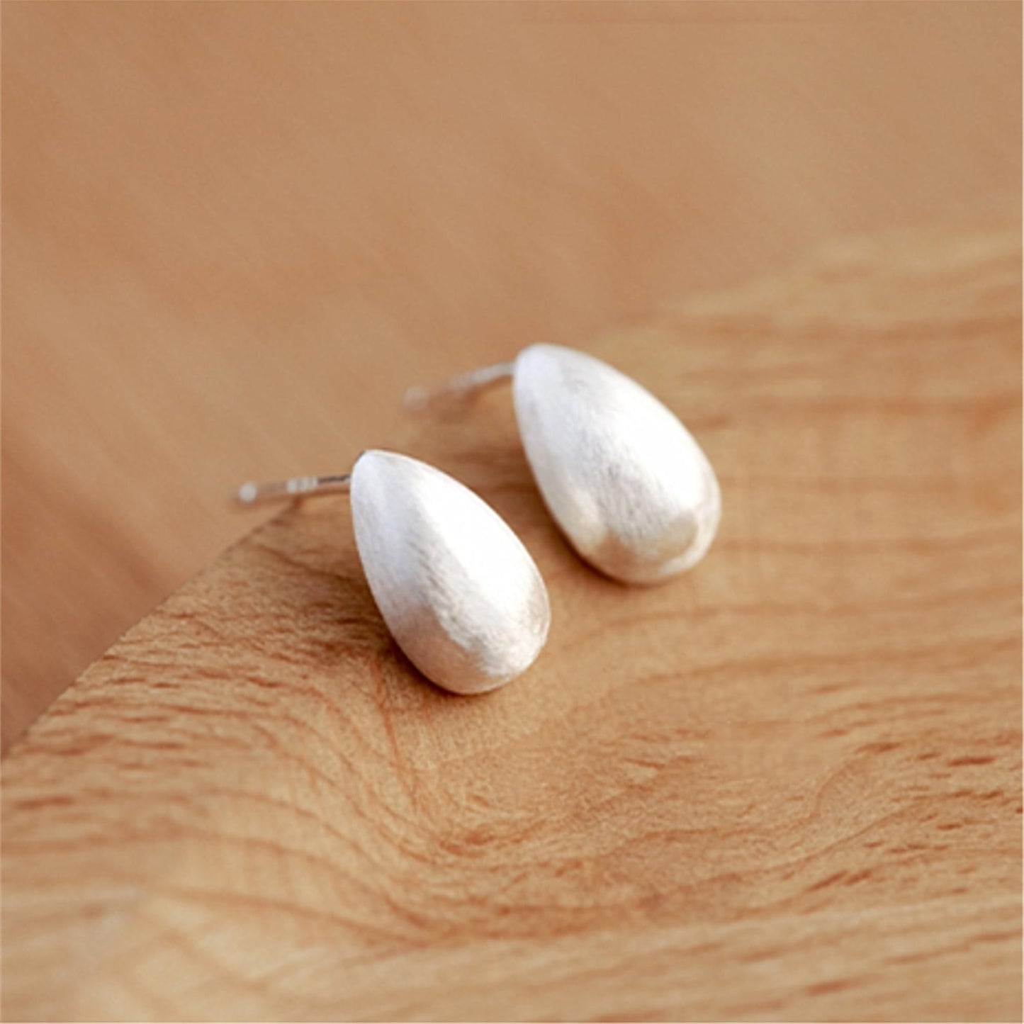 Teardrop stud earrings, silver-toned brushed caps on wooden surface