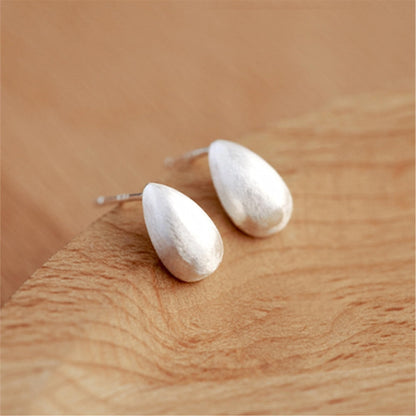 Teardrop stud earrings, silver-toned brushed caps on wooden surface